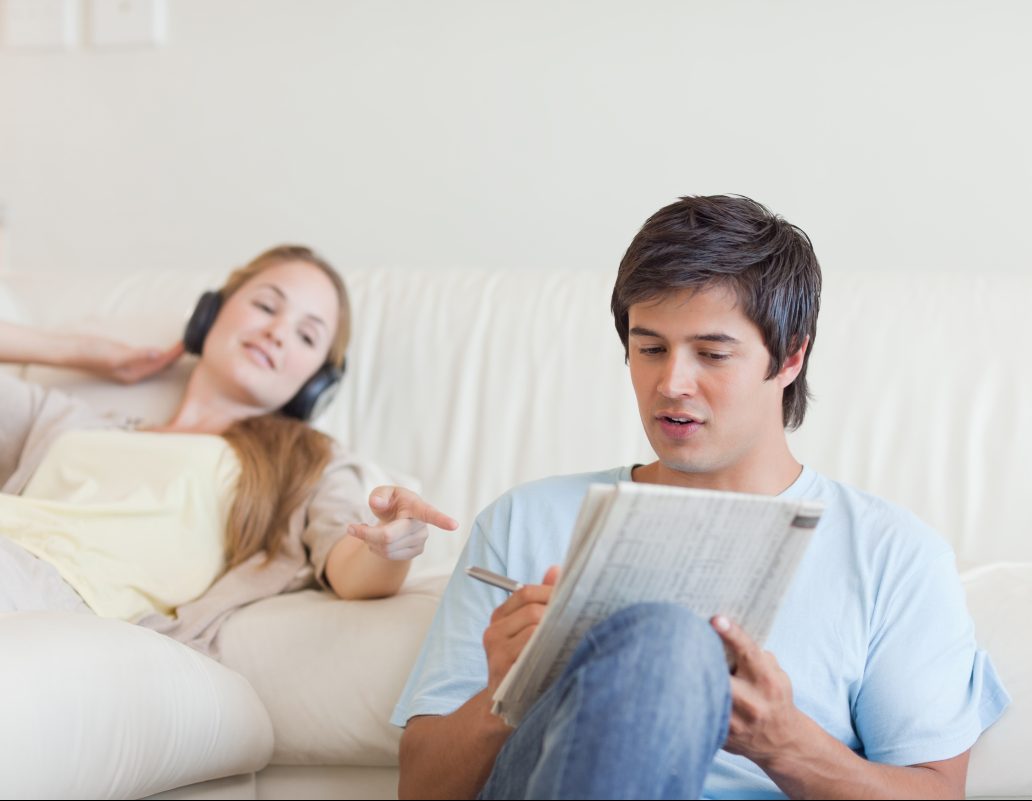 Woman helping her fiance to do crosswords while listening to music in their living room