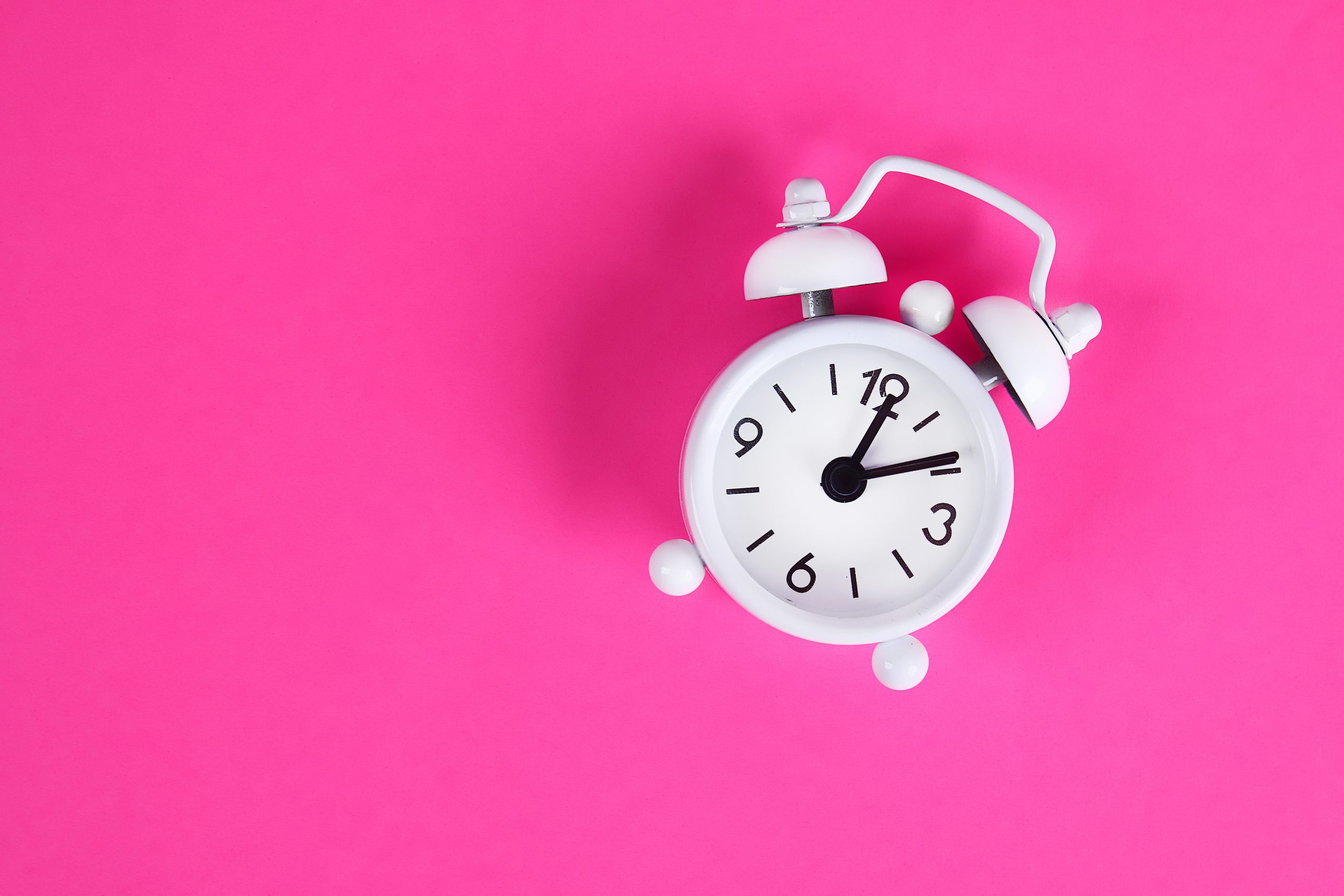 White alarm clock on pink background. Reminder. Space for copy. Minimal concept. Top view.