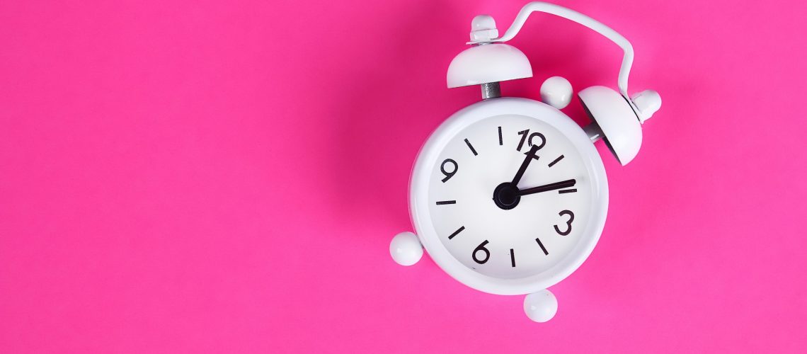 White alarm clock on pink background. Reminder. Space for copy. Minimal concept. Top view.