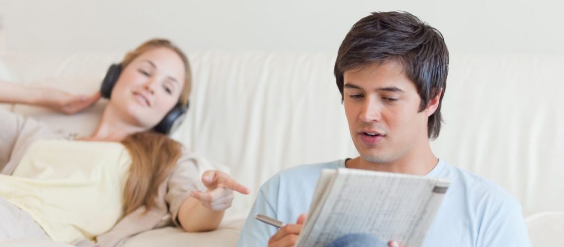 Woman helping her fiance to do crosswords while listening to music in their living room