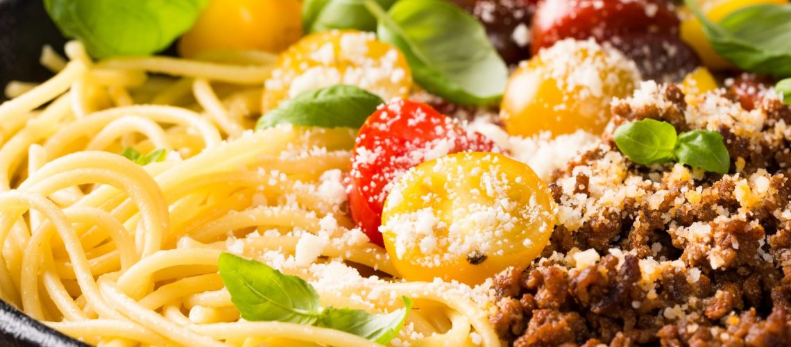 Delicious spaghetti Bolognaise or Bolognese with savory minced beef and cherry tomatoes garnished with parmesan cheese and basil in cost iron pan. Healthy italian food. Copy space.