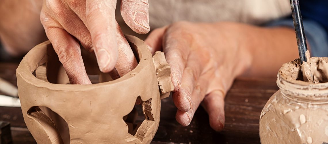 Close-up of a woman potter sculpts a brown clay candlestick  and makes hole in the form of stars for light on the background of a wooden table in the workshop