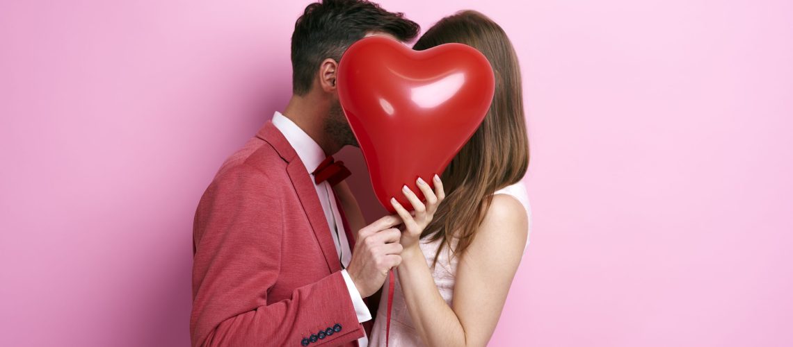 Affectionate couple covering face with balloon and kissing