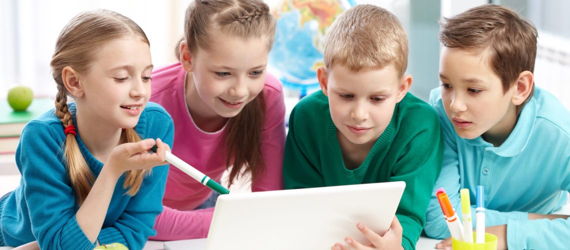 Portrait of smart schoolgirls and schoolboys looking at the laptop in classroom