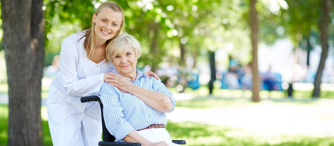 Pretty nurse and senior patient in a wheelchair looking at camera outside