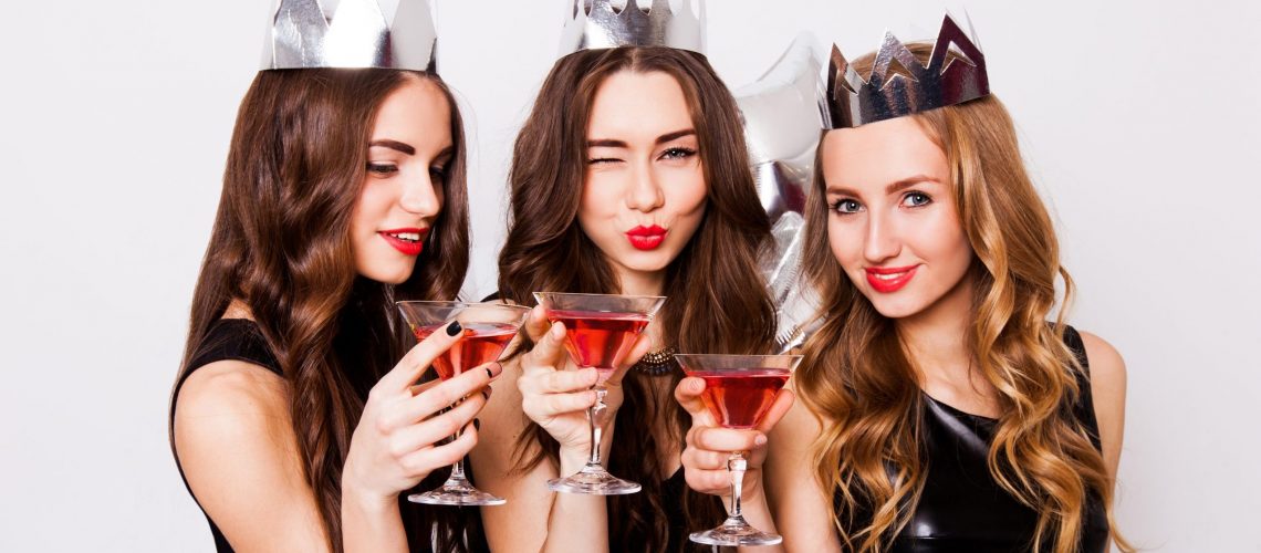 three-beautiful-elegant-women-celebrate-hen-party-and-drinking-cocktails-best-friends-wearing-black-evening-dress-crown-on-head-and-clink-glasses-bright-make-up-red-lips-inside