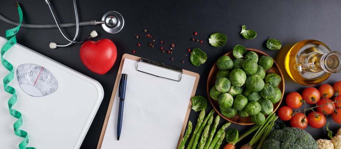 Weight loss scale with centimeter, stethoscope, Dumbbell, Clipboard, pen. Diet concept. Healthy food background. different fruits and vegetables, nuts. concept slimming diet fresh vegetables.