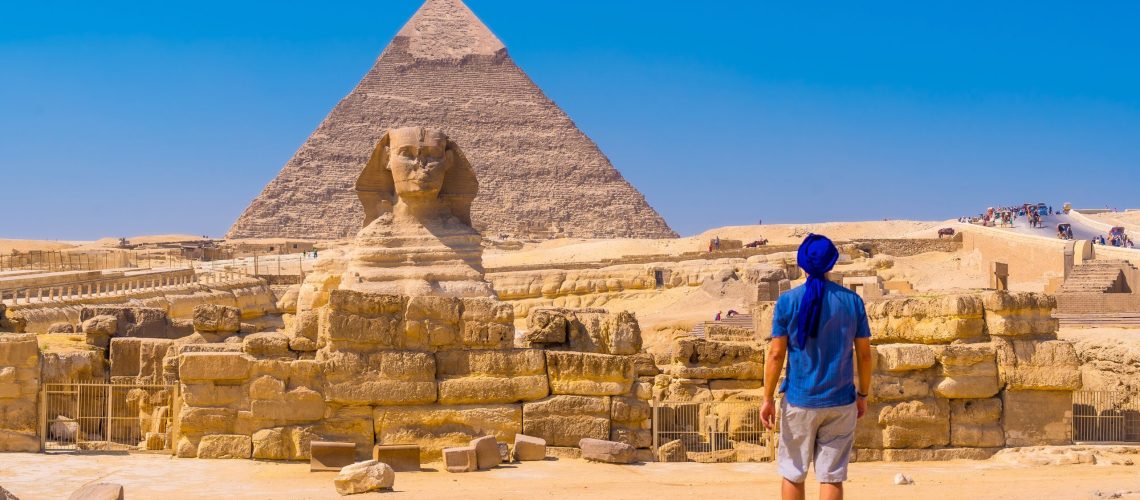 A young man walking towards the Great Sphinx of Giza and in the background the pyramid of Khafre,